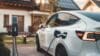 A photograph of an electric vehicle outside a house being charged up.