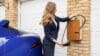 A woman is pictured plugging her electric vehicle plug into a charge point on the wall of a house.