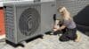 A female installer crouches down next to an Ideal Heating heat pump.