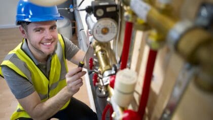 A smiling man in a hard hat and high vis vest working on some piping.