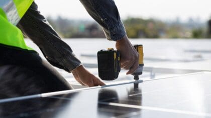 A close up of an installer's hands as they drill solar panels into place on a rooftop.