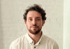 Man with beard wearing white shirt standing in front of white wall